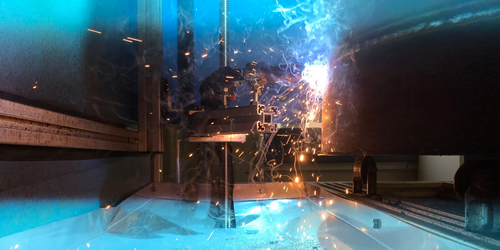 Welding arm working on a steel drum during a welding process with visible sparks and fumes